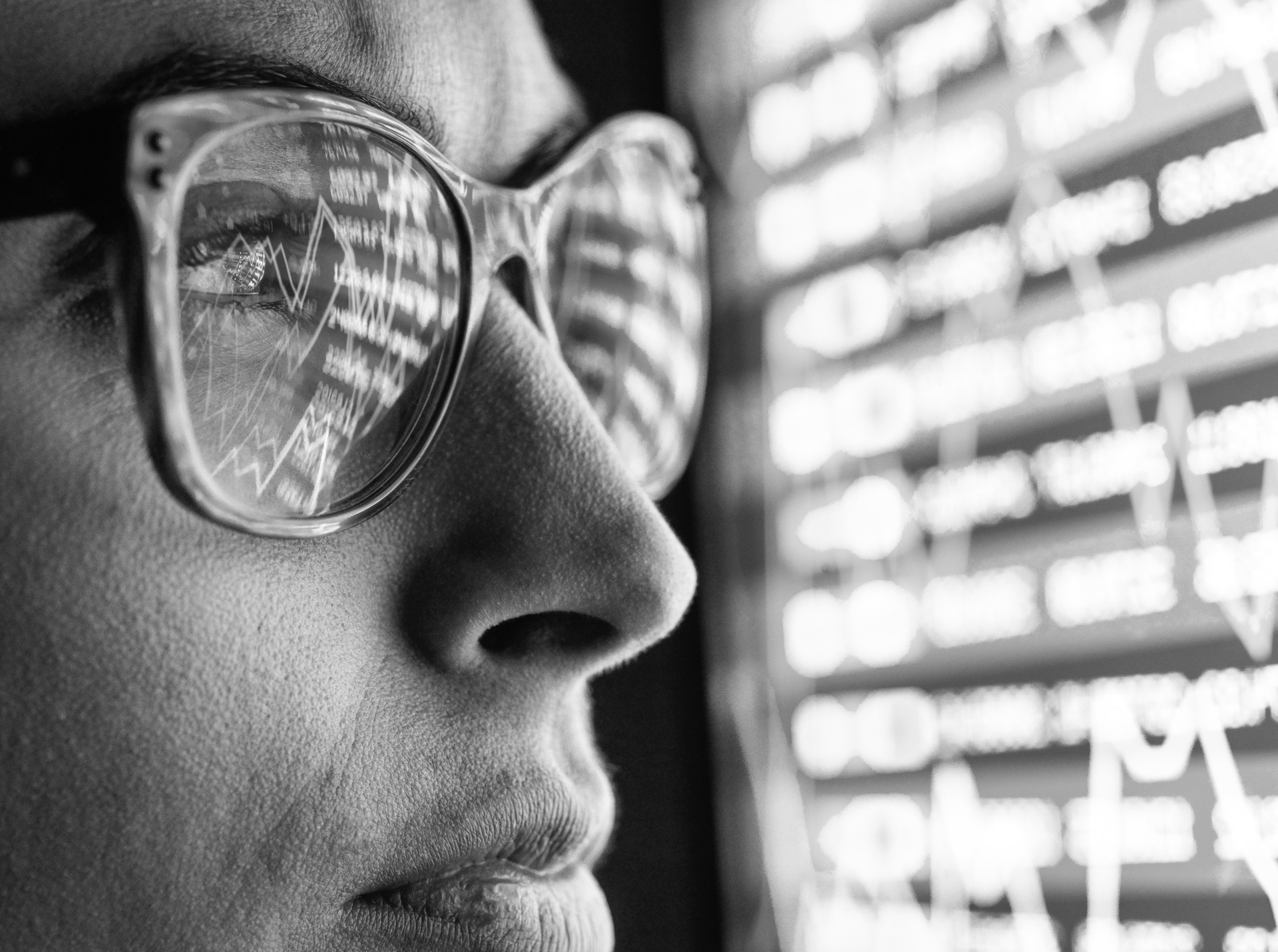 Person viewing financial market data and stock price charts on a screen, black and white image