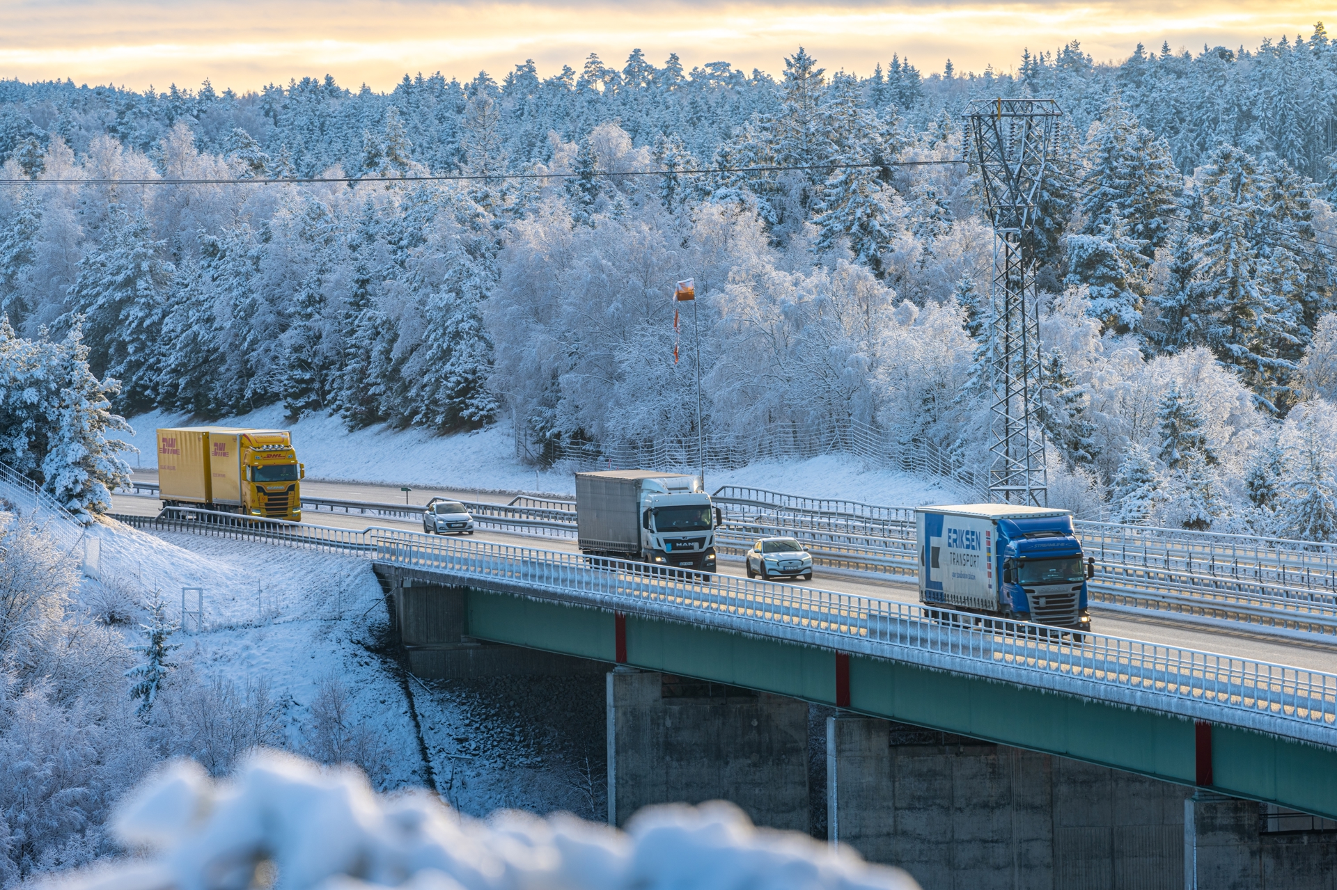  Trucks and cars crossing a bridge on a snow-covered highway.