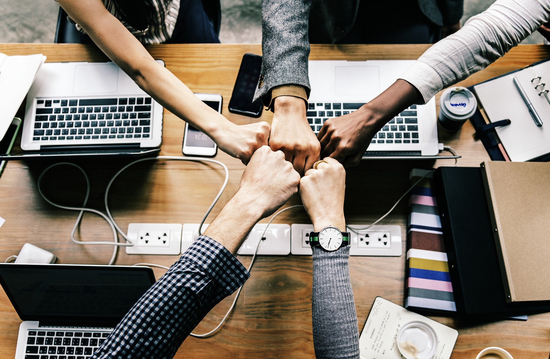 Five people bumping fists around a desk with laptops and work materials.