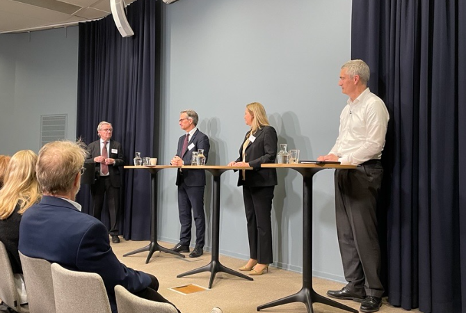 Four speakers participating in a panel discussion before a seated audience