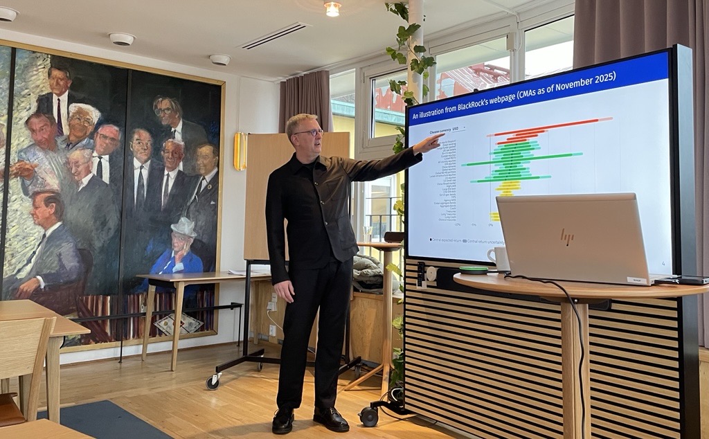 Presenter standing beside a screen displaying investment and market data charts